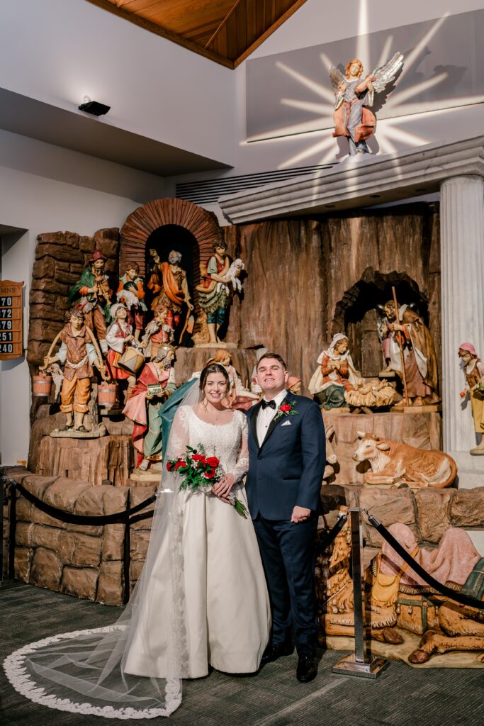 A bride and groom posed in front of a nativity scene during a Christmas themed wedding at St. Joseph Catholic Church in Herndon Virginia