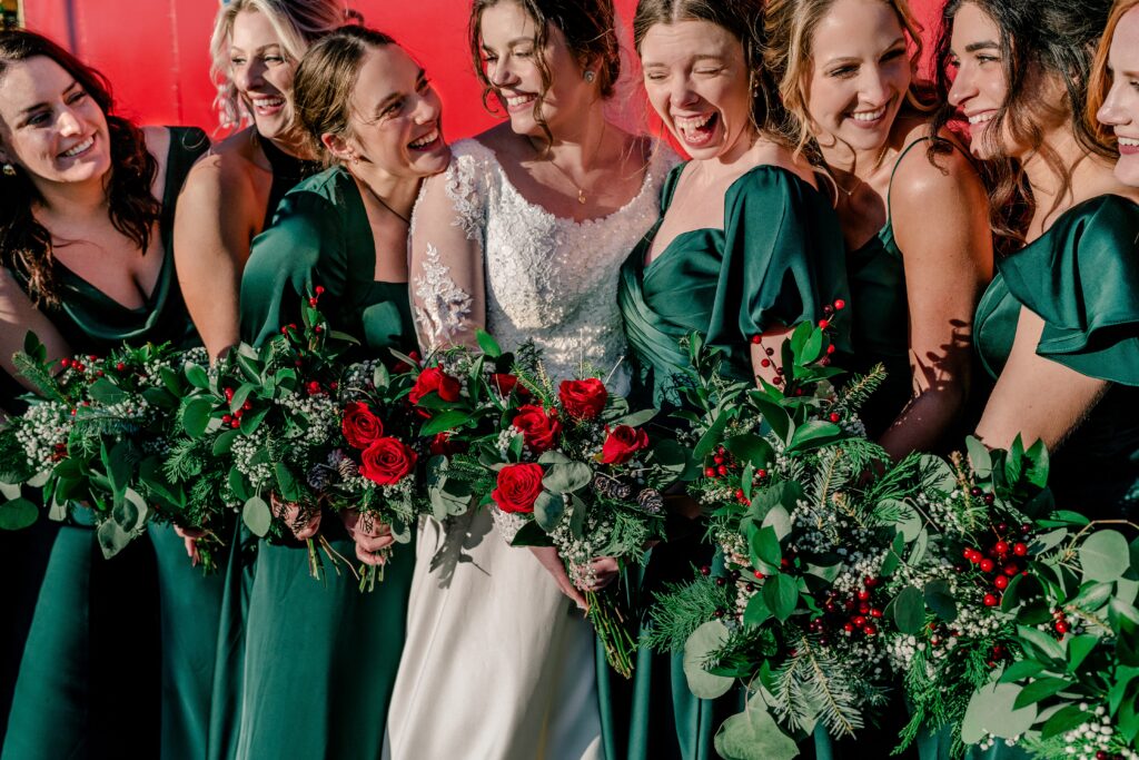 A bridal party laughing as they hold rose bouquets during a Christmas themed wedding in Herndon Virginia