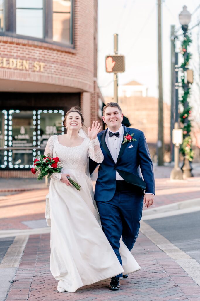 A bride and groom wave at friends as they cross the crosswalk