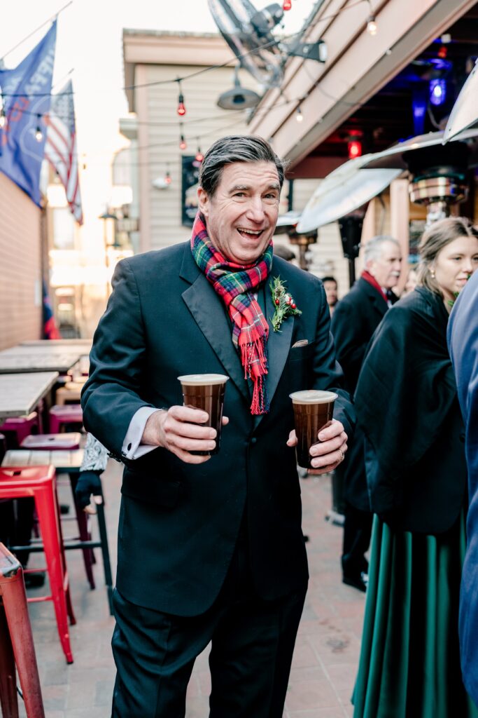 A man holding two drinks at an outdoor bar during a Christmas themed wedding in Herndon Virginia