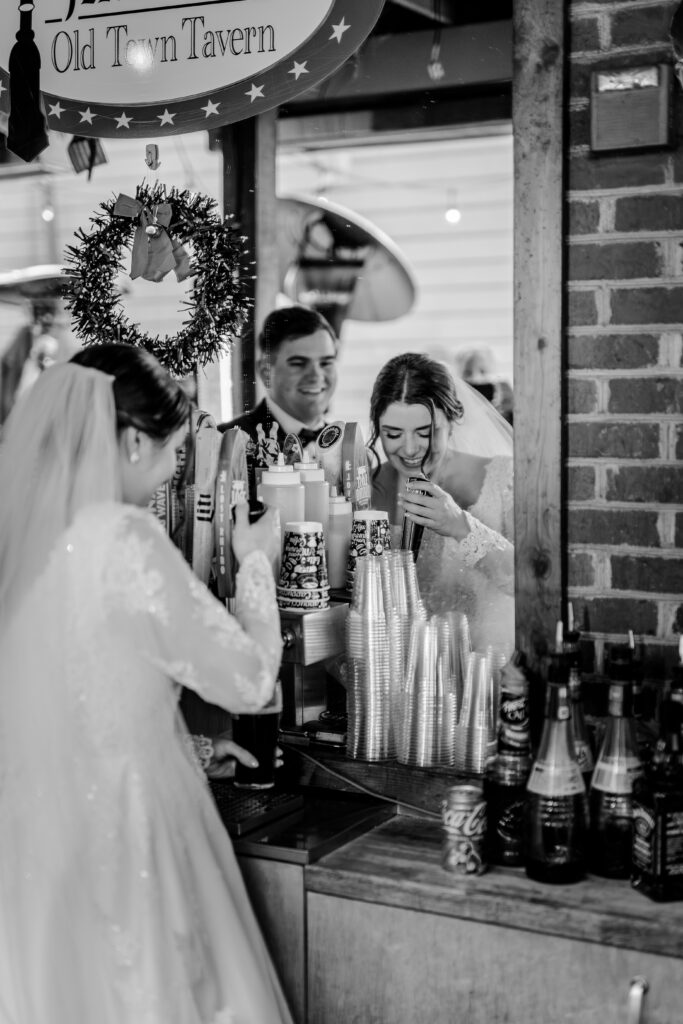 A bride and groom pour themselves drinks behind the bar on their wedding day