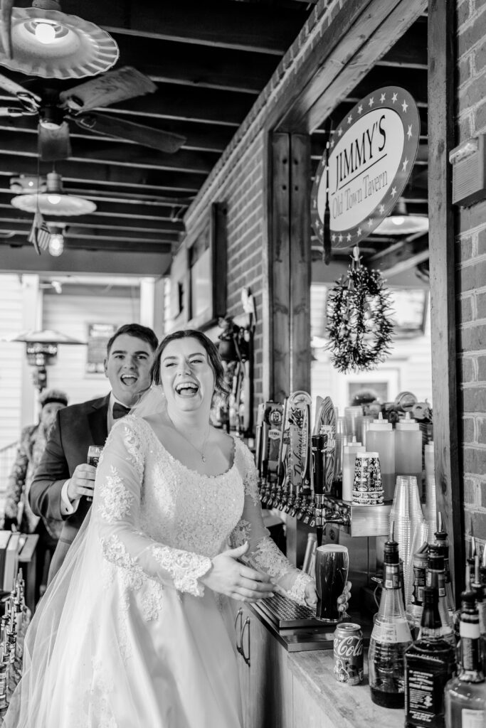 A bride and groom laugh as they pour their own drinks on their wedding day