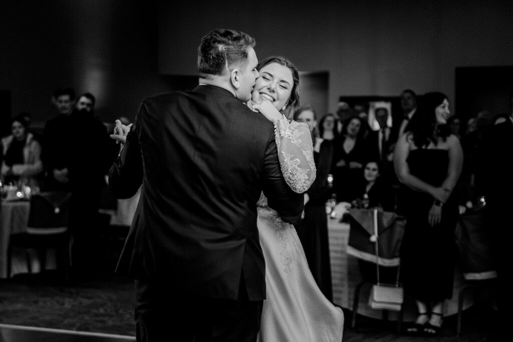 A groom kisses his bride as they dance together