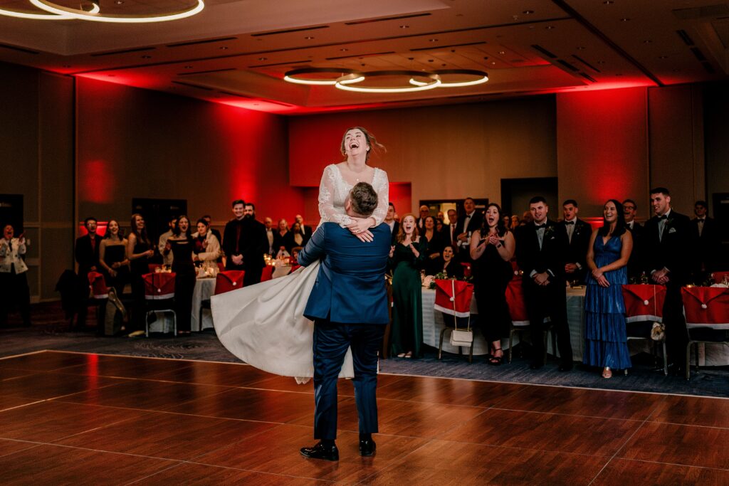 A bride laughs as her groom twirls her in the air