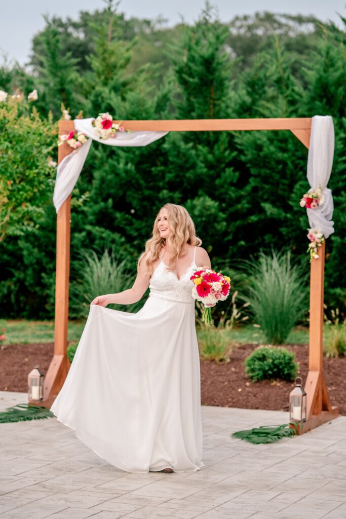 A bride posing for a bridal portrait in front of the ceremony arch at Halcyon Watson, a modern barn wedding venue in Leesburg Virginia