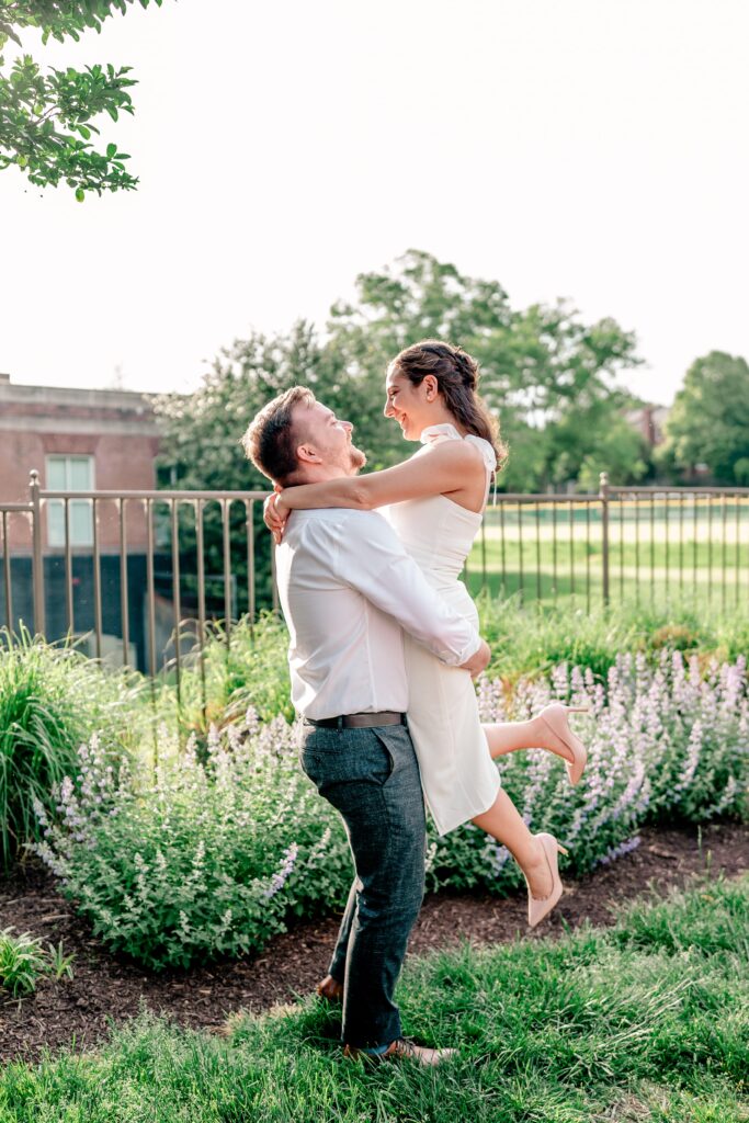 A couple shares a cute moment as he picks her up in golden hour light during their Georgetown DC engagement photos