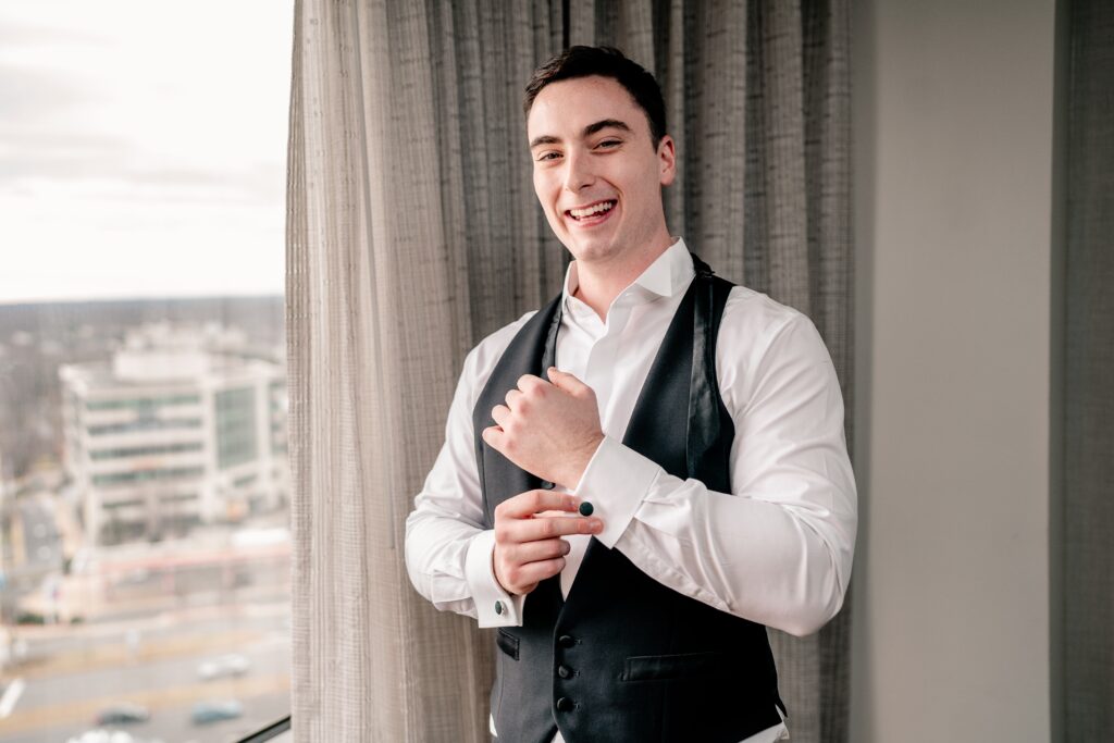A groom smiles for the camera as he gets dressed