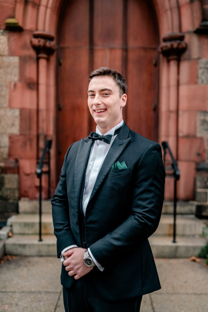 A groom smiles for a formal portrait outside the church