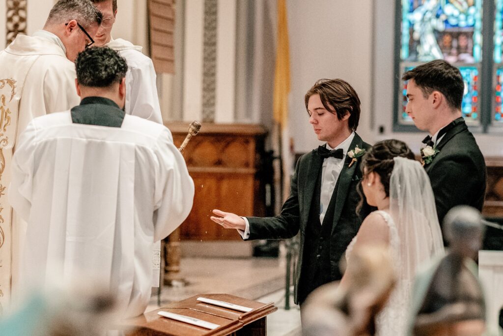 A groomsman holds out the rings for a blessing by Northern Virginia wedding photographer Beauty of the Soul Studio
