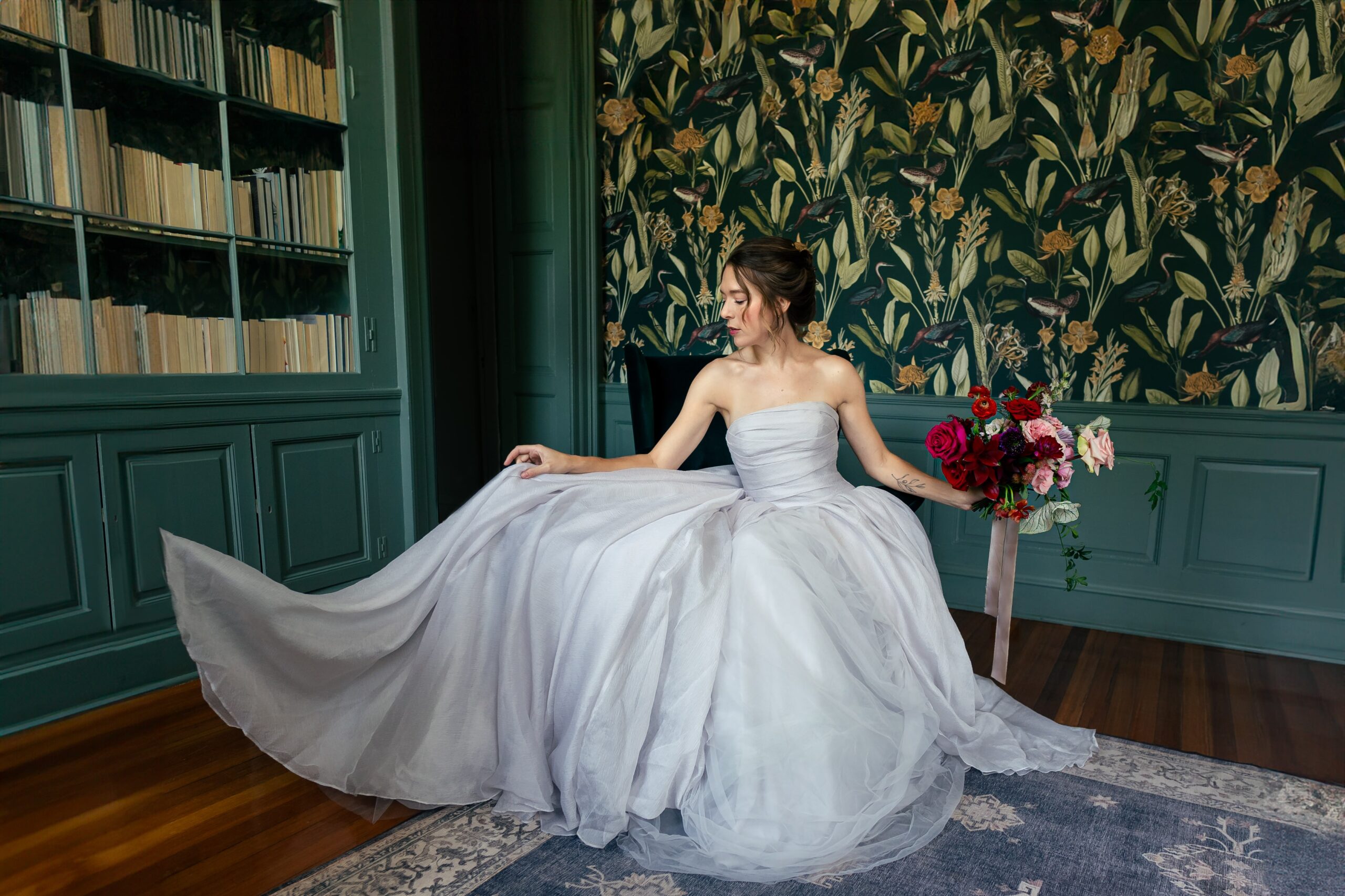 A bride wearing a gray Vera Wang textured organza ballgown sits in a moody library during a vintage inspired wedding styled shoot at Rust Manor House in Leesburg Virginia