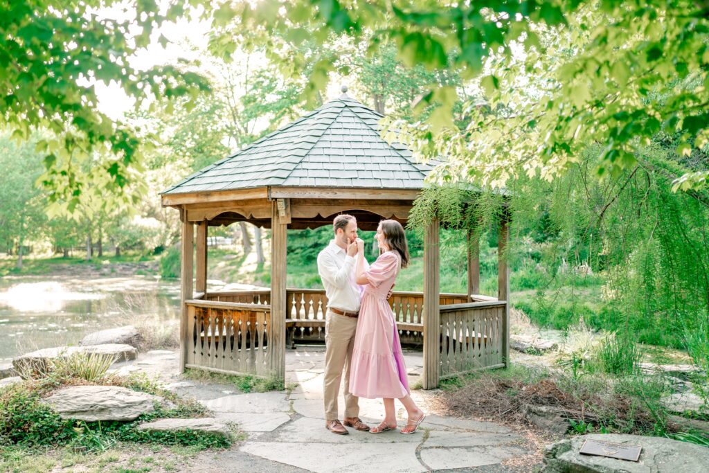 A man kisses his fiancee on the hand in front of a gazebo