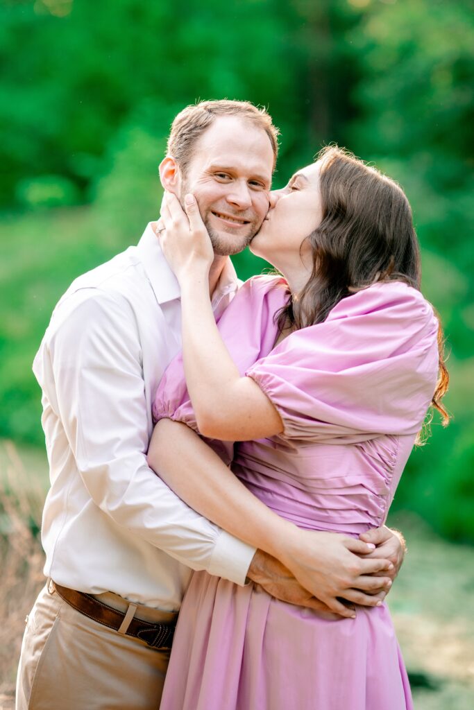 A woman kisses her beloved on the cheek during their engagement session at at one of the best garden venues in Northern Virginia