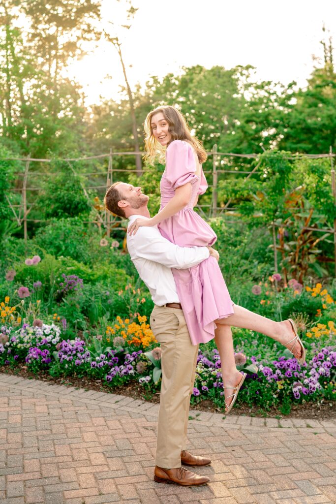 A man playfully lifts his fiancee off the ground during their engagement session at at one of the best garden venues in Northern Virginia