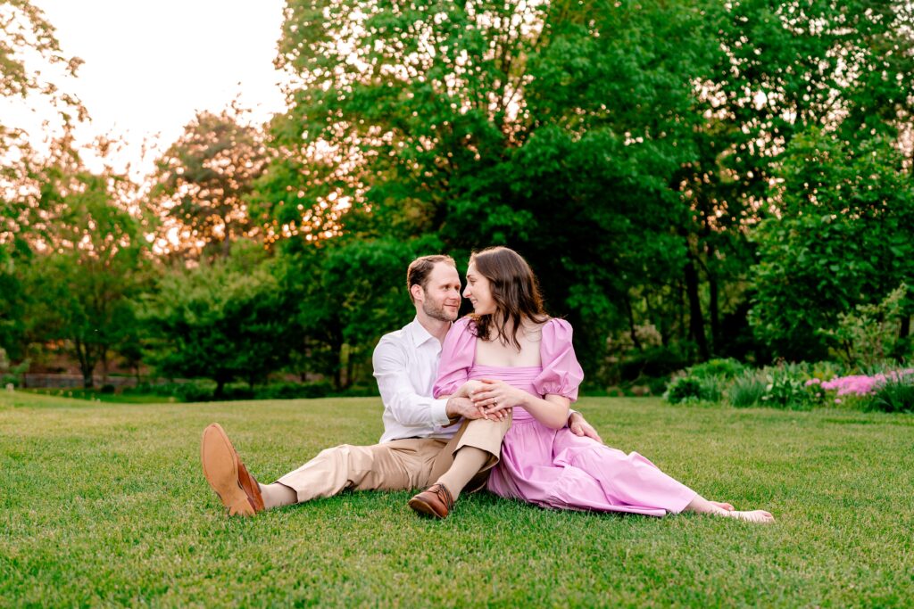 An engaged couple sitting on a lawn at sunset during their Green Spring Gardens photos