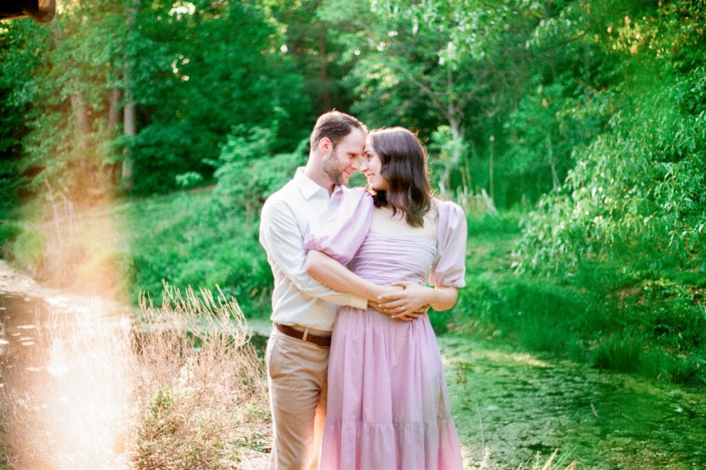 An engaged couple poses forehead to forehead in front of a pond