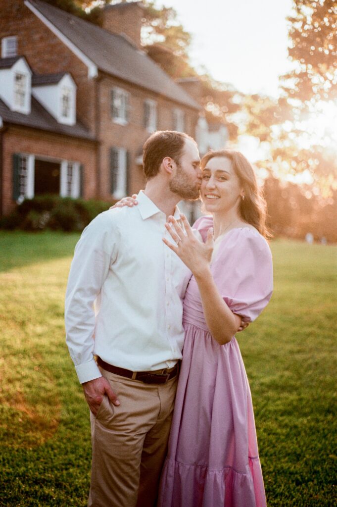 A woman shows off her engagement ring as her fiance kisses her cheek
