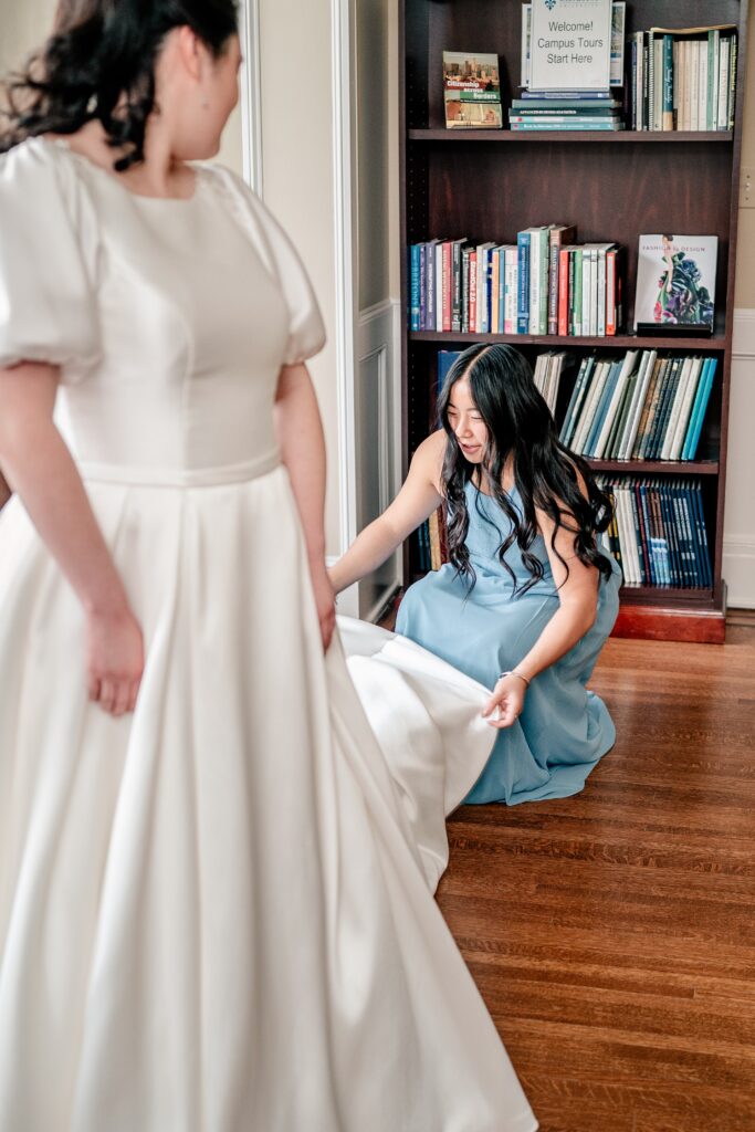 A bridesmaid fluffs the bride's train as she's getting ready