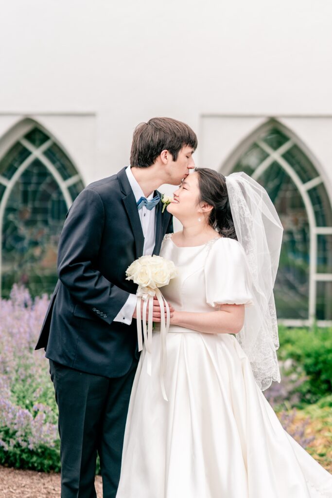 A groom kisses his bride on the forehead