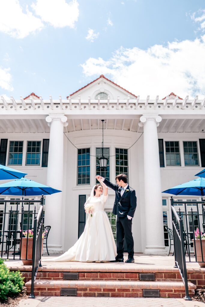 A groom twirls his bride on a sunny day