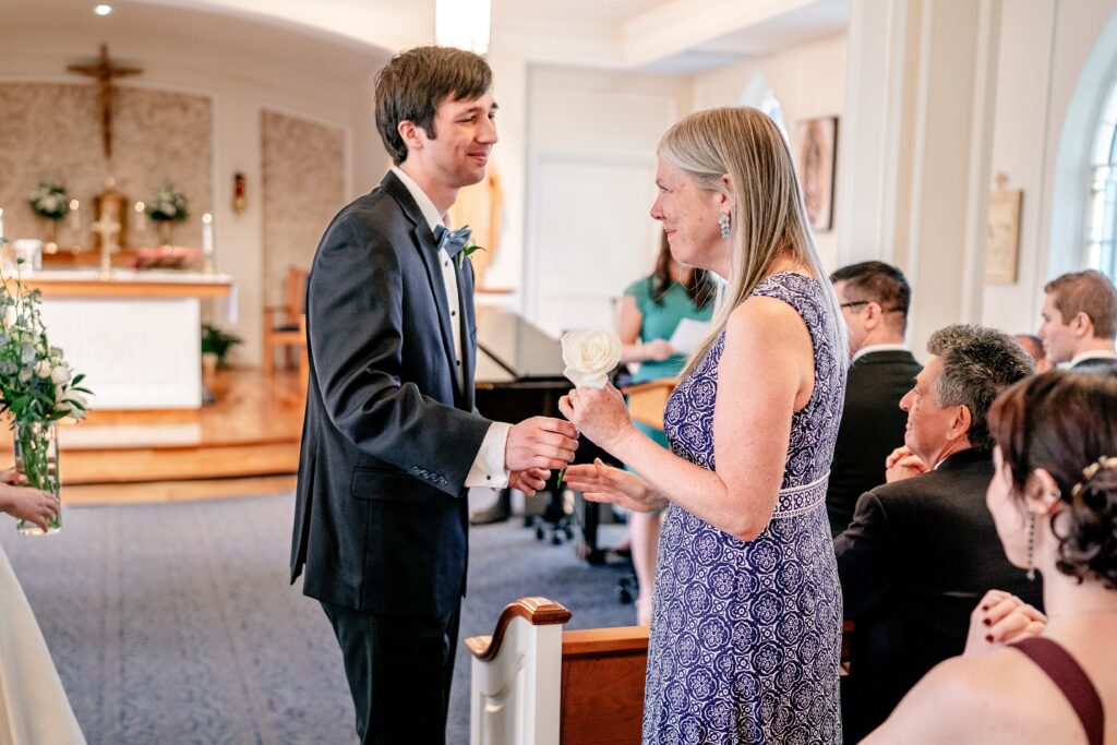A groom handing his mother a rose during his Catholic wedding