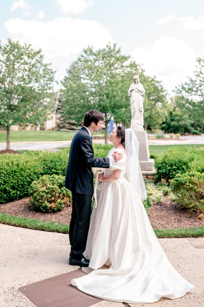 A bride and groom sharing a private moment in front of the Mary statue on campus after their Marymount University wedding