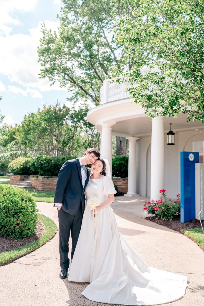 A bride and groom pose for a classic portrait in front of the chapel for their Marymount University wedding
