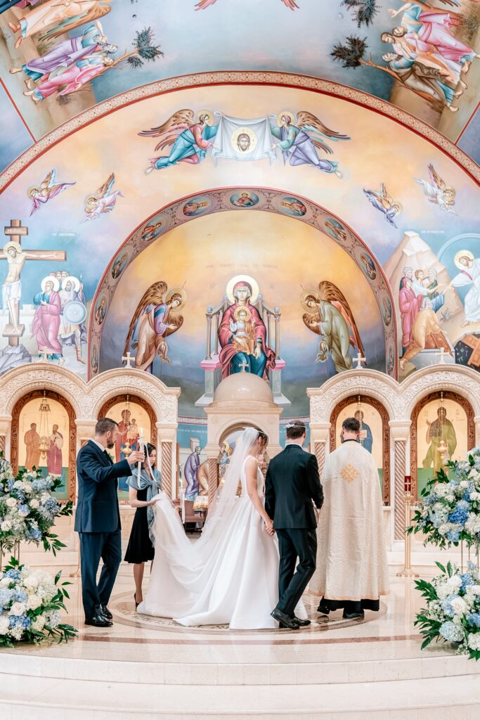 A bride and groom walking around the table with their priest and their sponsors for a Greek Orthodox wedding ceremony