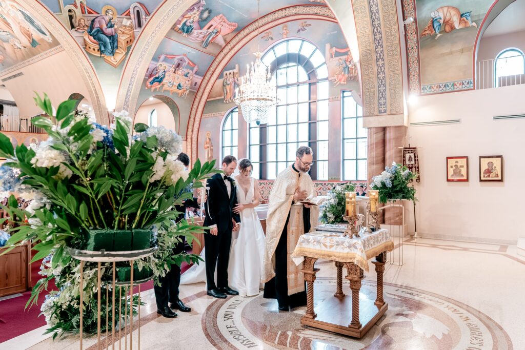 A wide view from the front of the church of a bride and groom and the priest during a Sts. Peter and Paul Antiochian Orthodox Church wedding in Potomac, Maryland