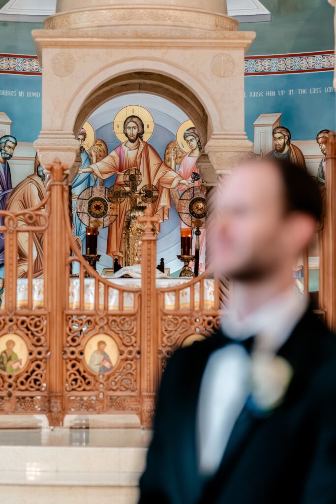 A fresco of Jesus behind the altar of a church with the groom in the foreground in a portrait by a colorful wedding photographer