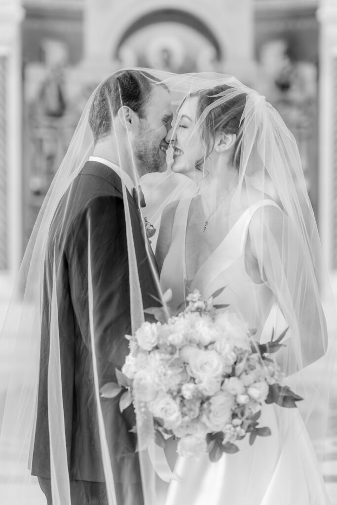 A bride and groom laughing together while under her veil