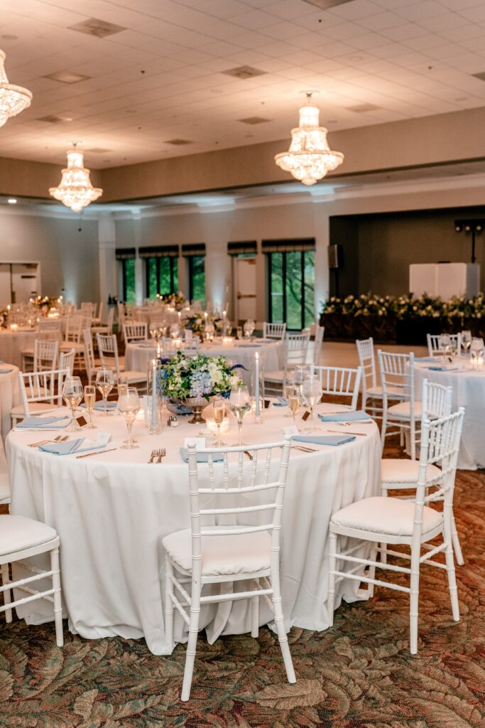A wedding reception in a ballroom with white chiavari chairs and blue hydrangea arrangements