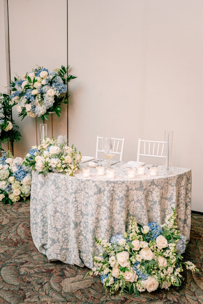 A sweetheart table with a floral blue tablecloth and large hydrangea arrangements