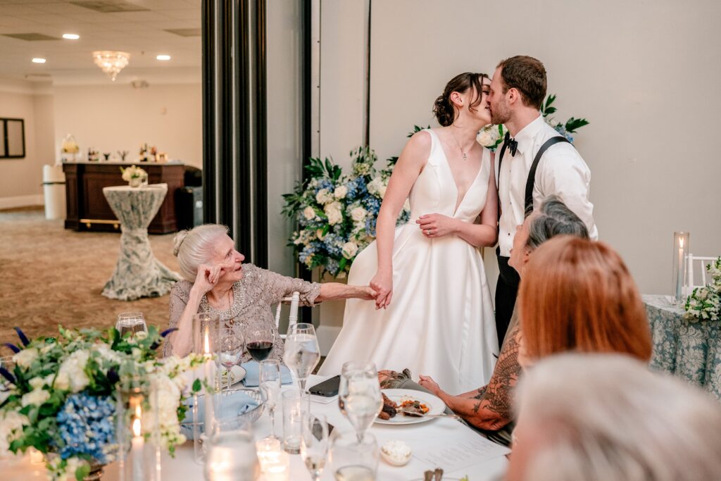 A bride and groom sharing a kiss as she holds her grandmother's hand for their colorful wedding photographer