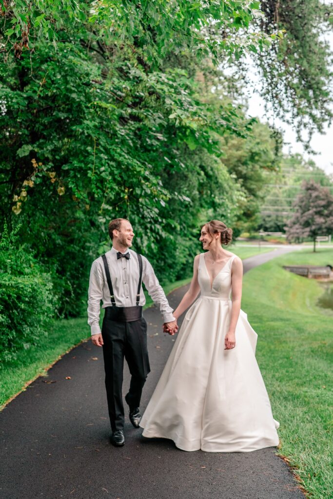 A bride and groom walking hand in hand together down a paved path