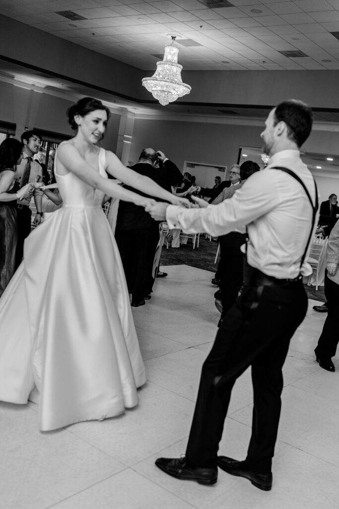 A bride and groom holding hands as they dance with their guests at the reception