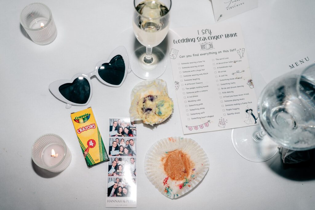 A late night flat lay featuring heart shaped sunglasses, drinks, a scavenger hunt card, crayons, cupcake wrappers, and a photobooth film strip during a Sts. Peter and Paul Antiochian Orthodox Church wedding in Potomac, Maryland