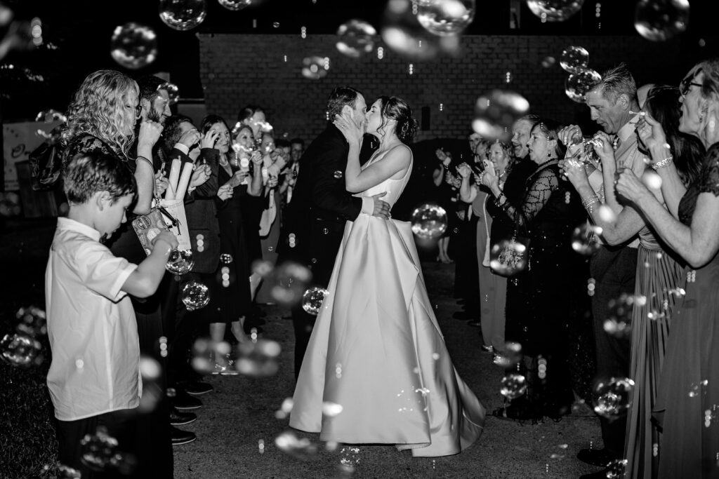 A bride and groom sharing a kiss during their bubble sendoff with their colorful wedding photographer