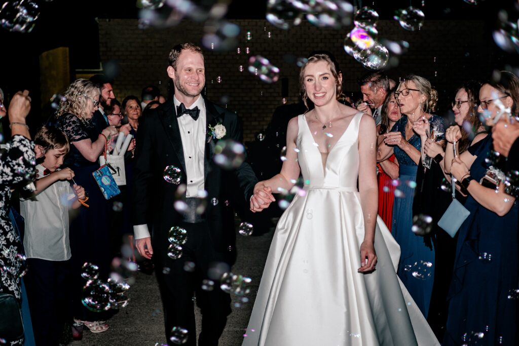 A bride and groom smiling as they walk through their bubble send off
