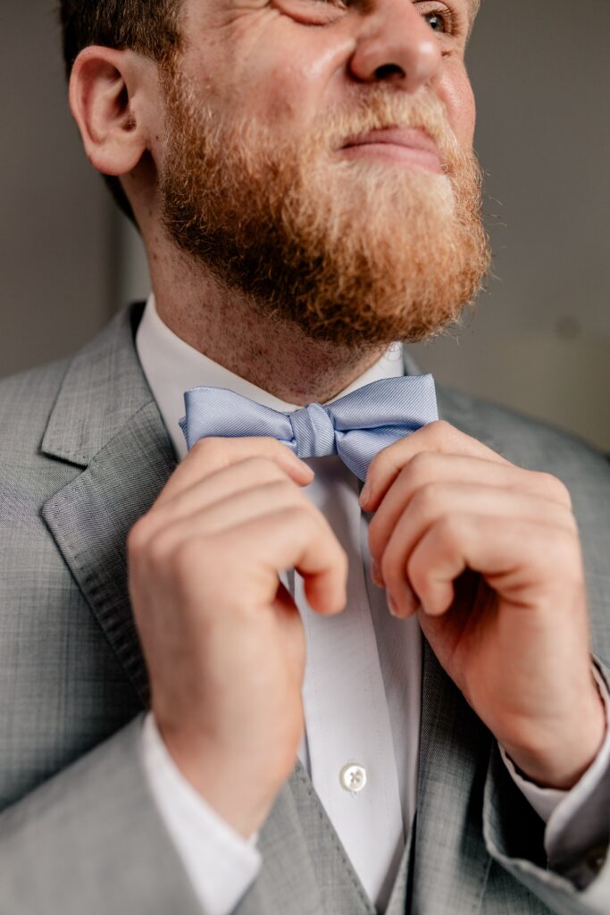 A groom straightening his bow tie with his Catholic wedding photographer