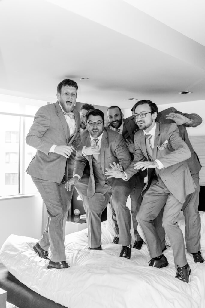 A group of groomsmen jumping on the hotel bed
