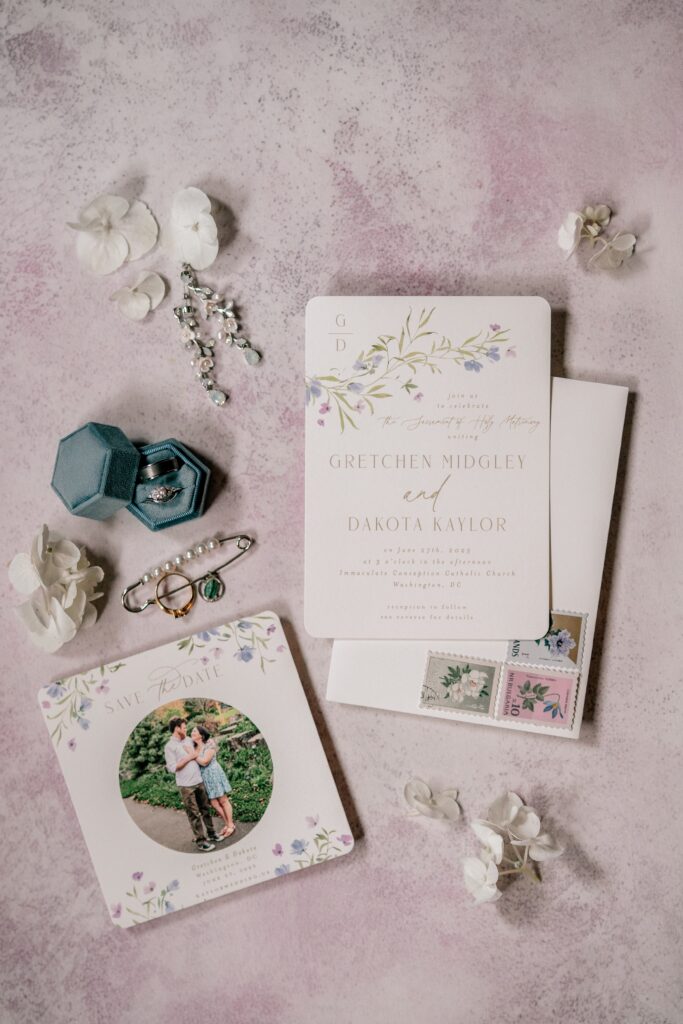 A flat lay of details featuring a pink background and floral invitations by a Washington DC wedding photographer