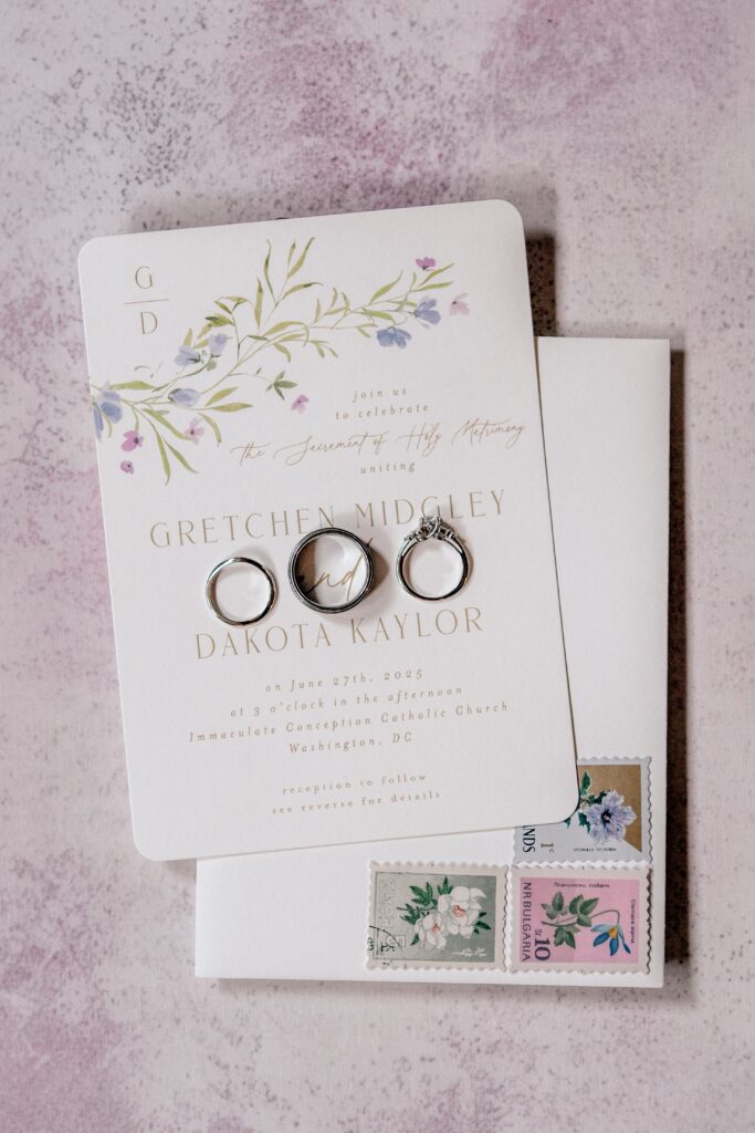 A wedding invitation on a pink background with rings on top