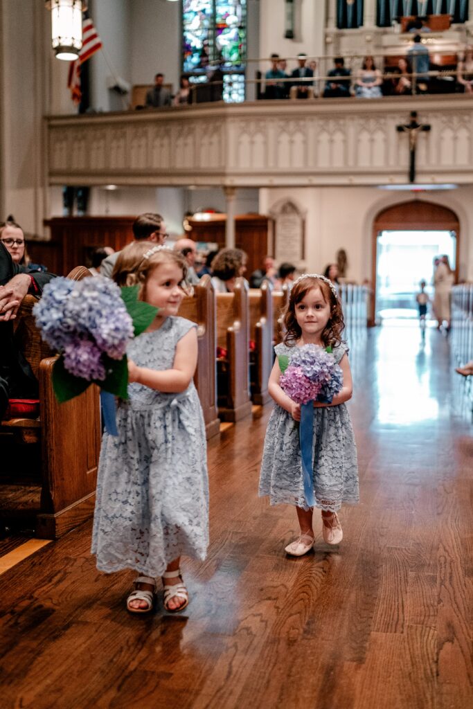 A pair of flower girls walking toward the Catholic wedding photographer