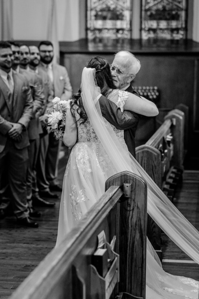 A bride and her father sharing a hug after he walked her down the aisle
