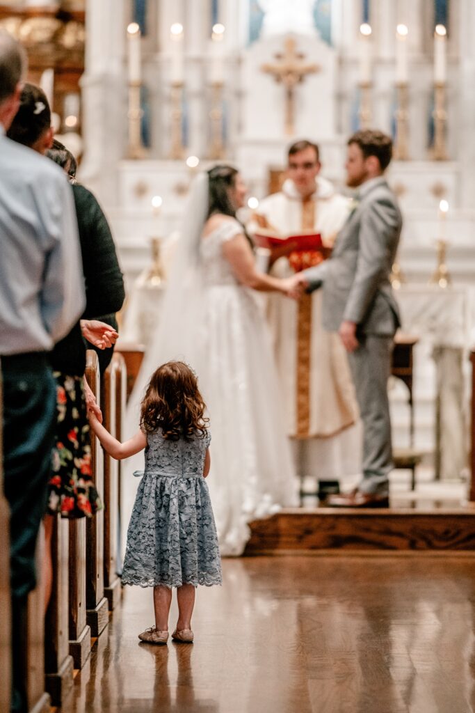 A bridesmaid watching the bride and groom exchange vows during an Immaculate Conception Church wedding