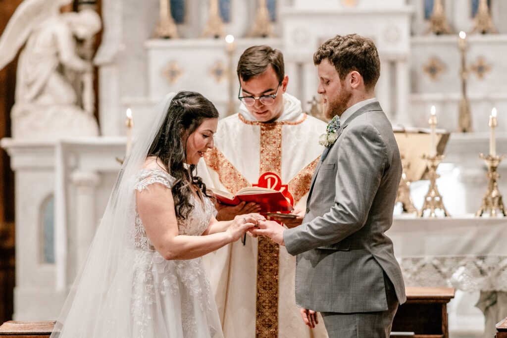 A bride and groom exchanging rings in front of their Catholic wedding photographer