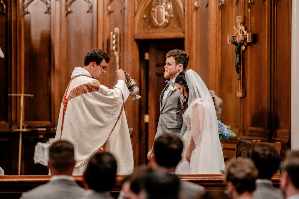 A priest swinging incense in front of a bride and groom