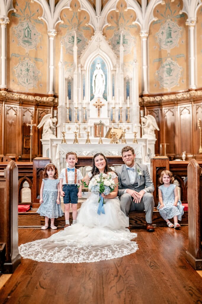 A bride and groom posing with children for their Catholic wedding photographer