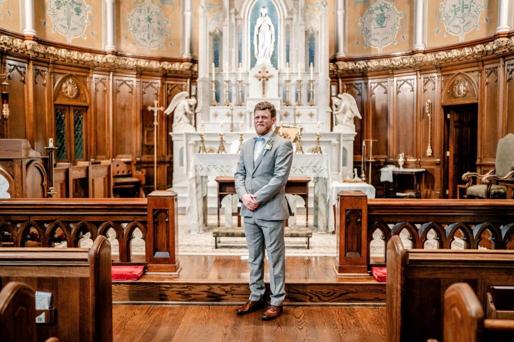 A groom posing in front of the altar for his Catholic wedding photographer
