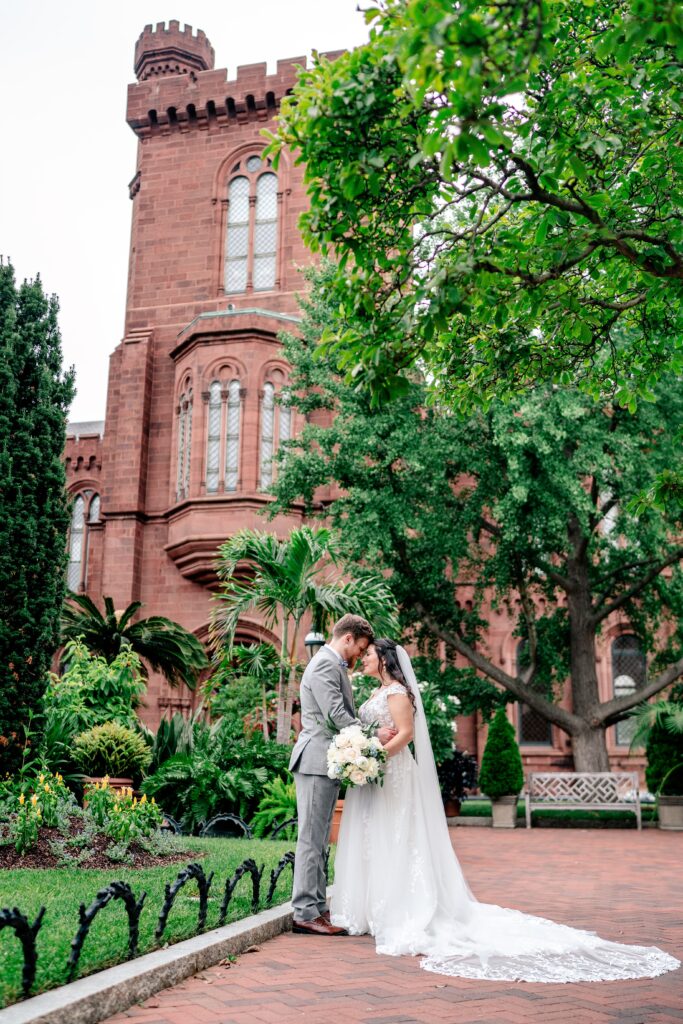 A bride and groom posed in front of the Smithsonian Castle in the Enid A. Haupt Gardens